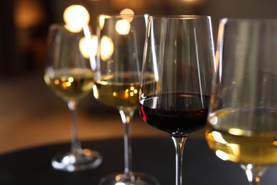 Different tasty wines in glasses on black table against blurred lights, closeup