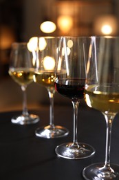 Different tasty wines in glasses on black table against blurred lights, closeup