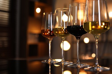 Photo of Different tasty wines in glasses on table against blurred lights, closeup. Space for text