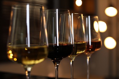 Photo of Different tasty wines in glasses against blurred lights, closeup
