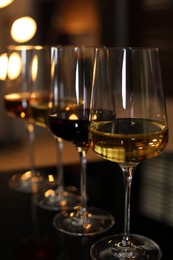 Photo of Different tasty wines in glasses on table against blurred lights, closeup