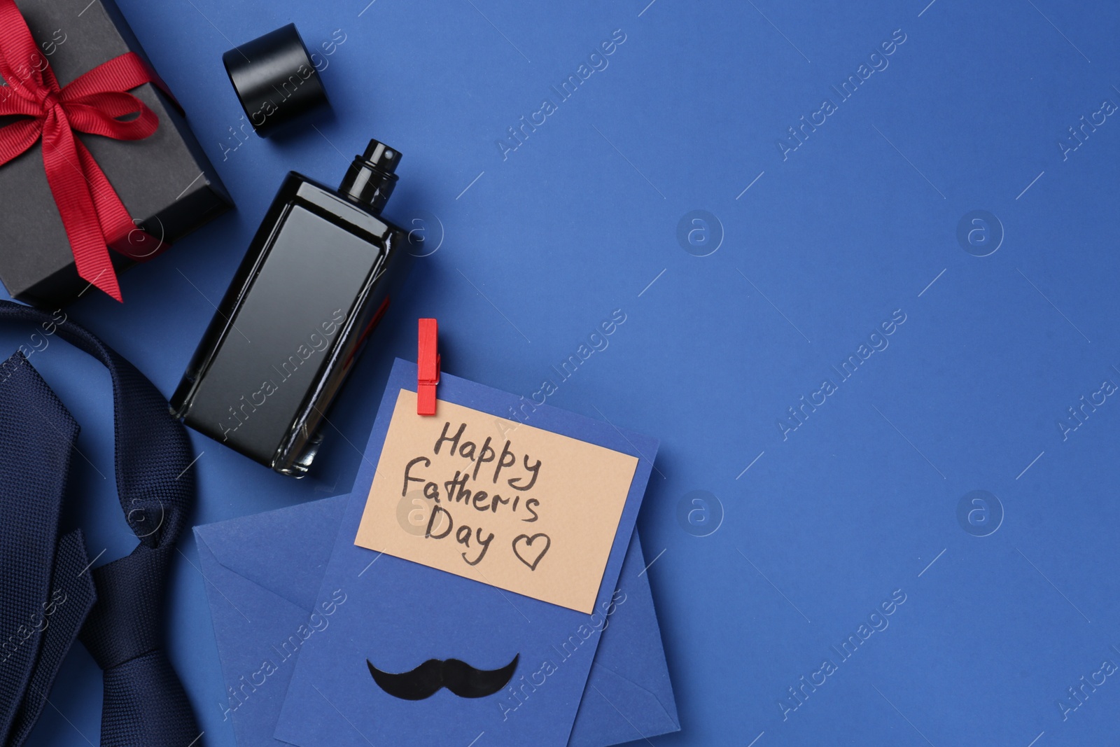 Photo of Greeting card with phrase Happy Father's Day, envelope, bottle of perfume, tie and gift on blue background, flat lay. Space for text