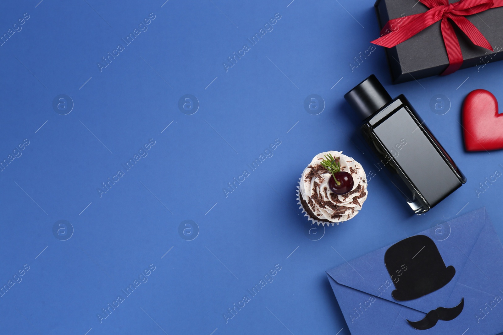 Photo of Happy Father's Day. Creative envelope, bottle of perfume, gift, decorative heart and cupcake on blue background, flat lay. Space for text