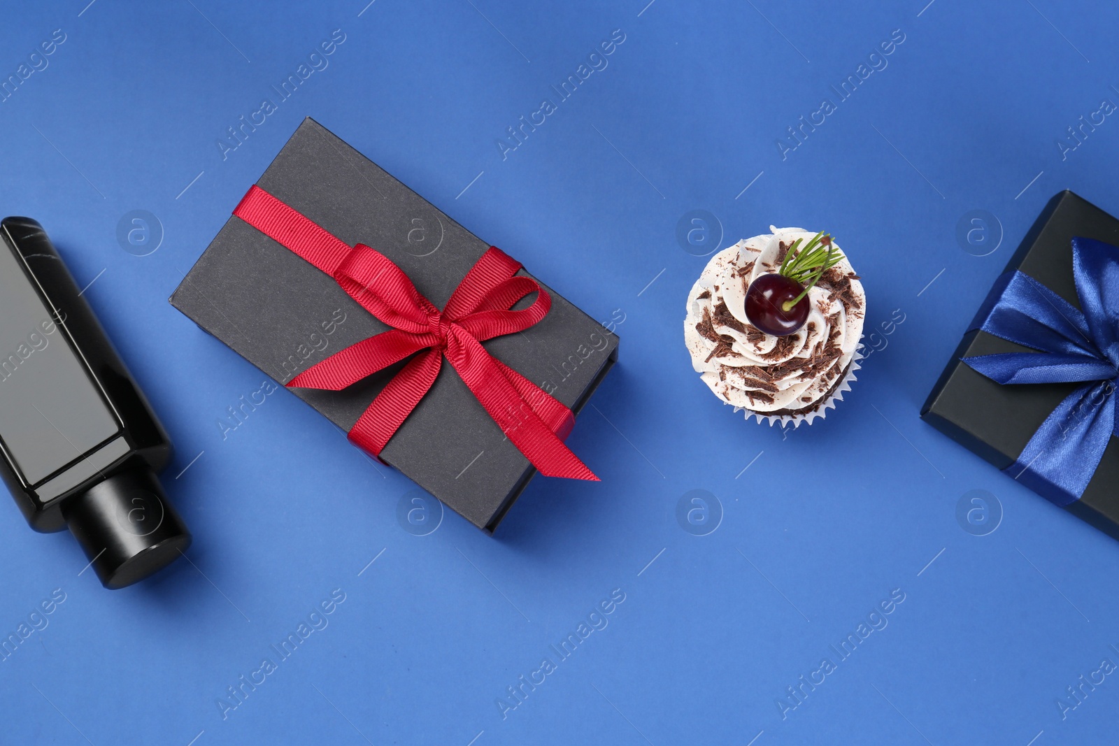 Photo of Happy Father's Day. Perfume bottle, gift boxes and cupcake on blue background, flat lay