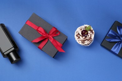 Photo of Happy Father's Day. Perfume bottle, gift boxes and cupcake on blue background, flat lay