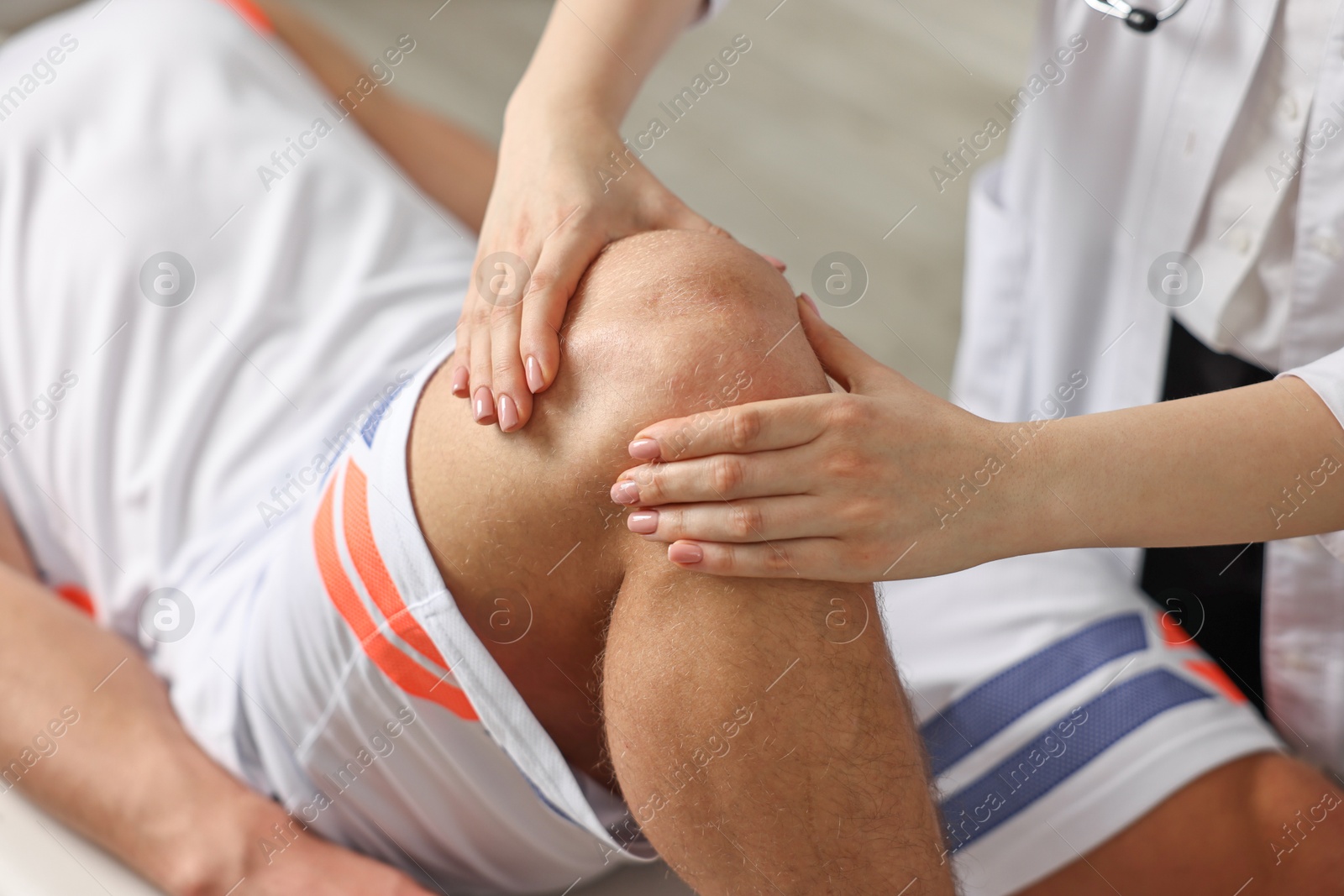 Photo of Sports injury. Doctor examining patient's knee in hospital, closeup