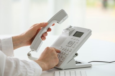 Photo of Assistant dialing number on telephone against blurred background, closeup