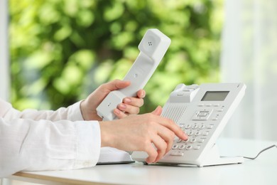 Assistant dialing number on telephone against blurred green background, closeup