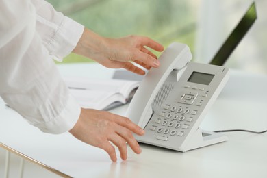 Photo of Assistant taking telephone handset at white table, closeup