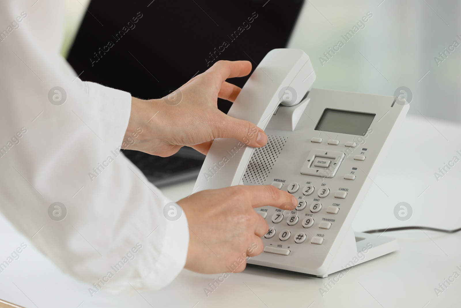 Photo of Assistant taking telephone handset at white table, closeup