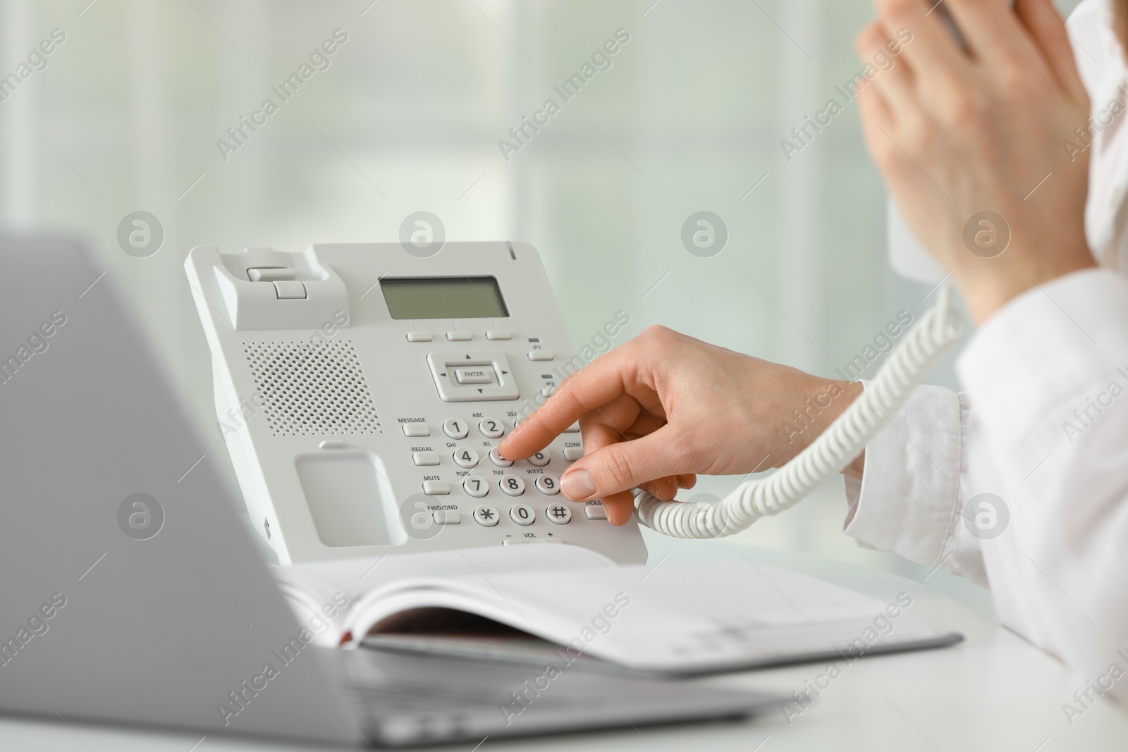 Photo of Assistant dialing number on telephone at table in office, closeup