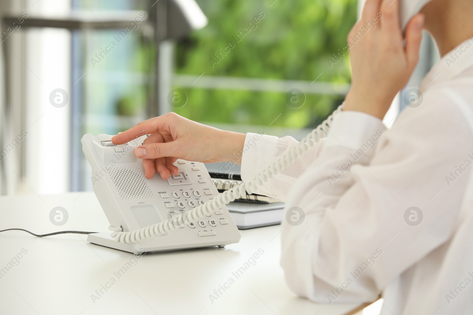 Photo of Assistant with telephone handset at white table, closeup