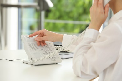 Assistant with telephone handset at white table, closeup