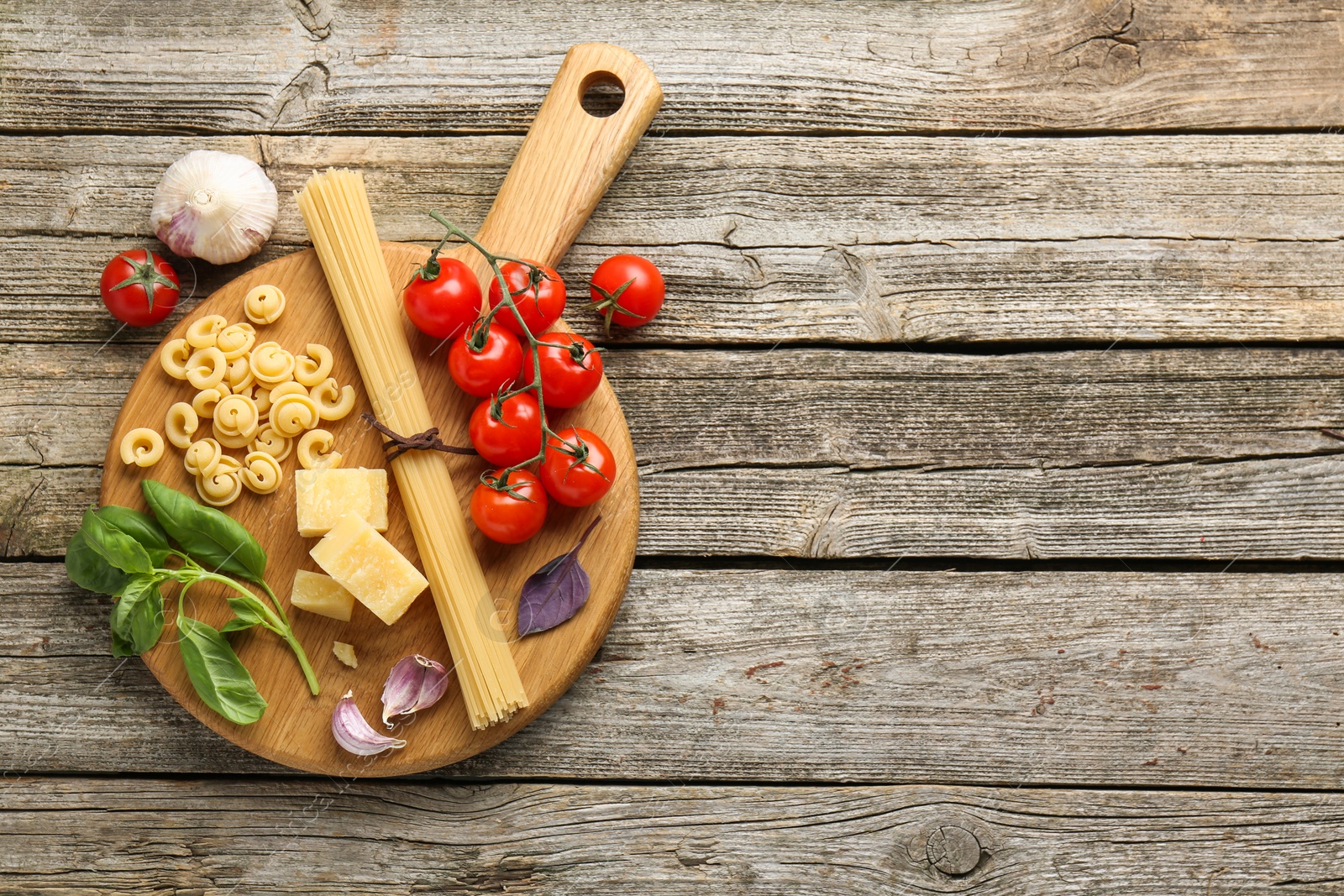 Photo of Board with different types of pasta and products on wooden table, flat lay. Space for text