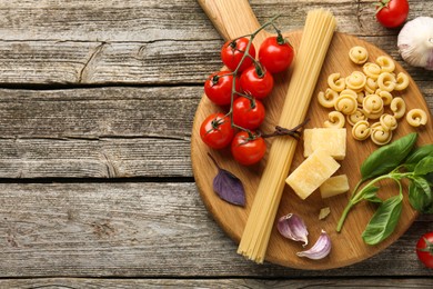 Board with different types of pasta and products on wooden table, flat lay. Space for text