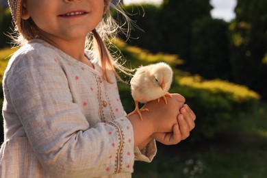Photo of Cute little girl with chick outdoors, closeup. Baby animal