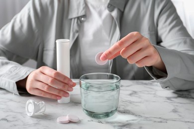 Photo of Woman putting effervescent pill into glass of water at white marble table, closeup