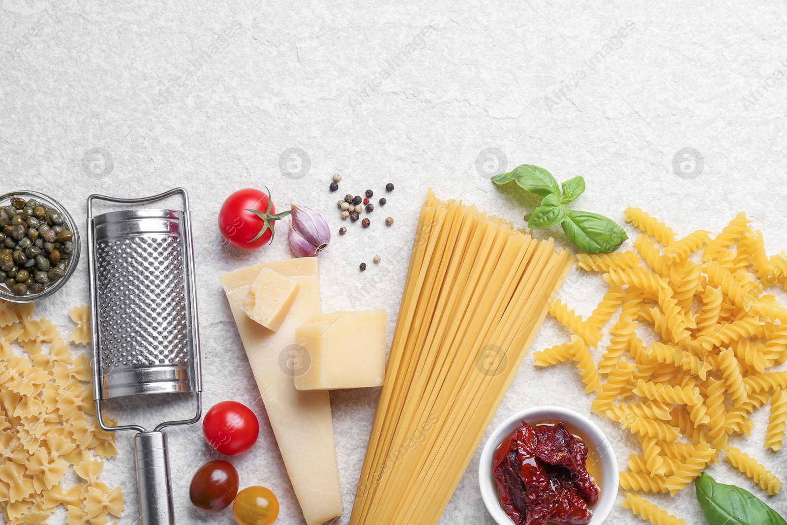 Photo of Different types of pasta, grater, spices and products on light table, flat lay. Space for text