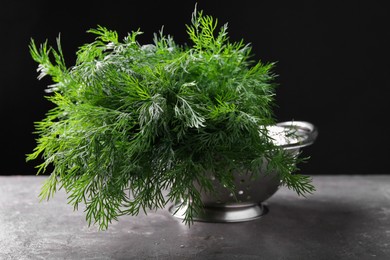 Photo of Fresh wet dill in colander on grey textured table against black background, closeup