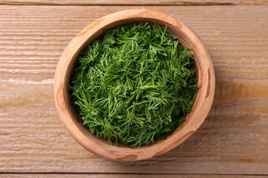 Photo of Fresh cut dill in bowl on wooden table, top view