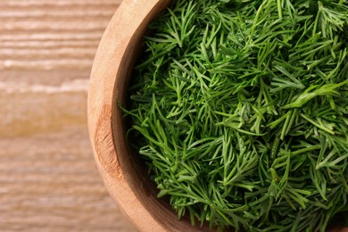 Photo of Fresh cut dill in bowl on wooden table, top view