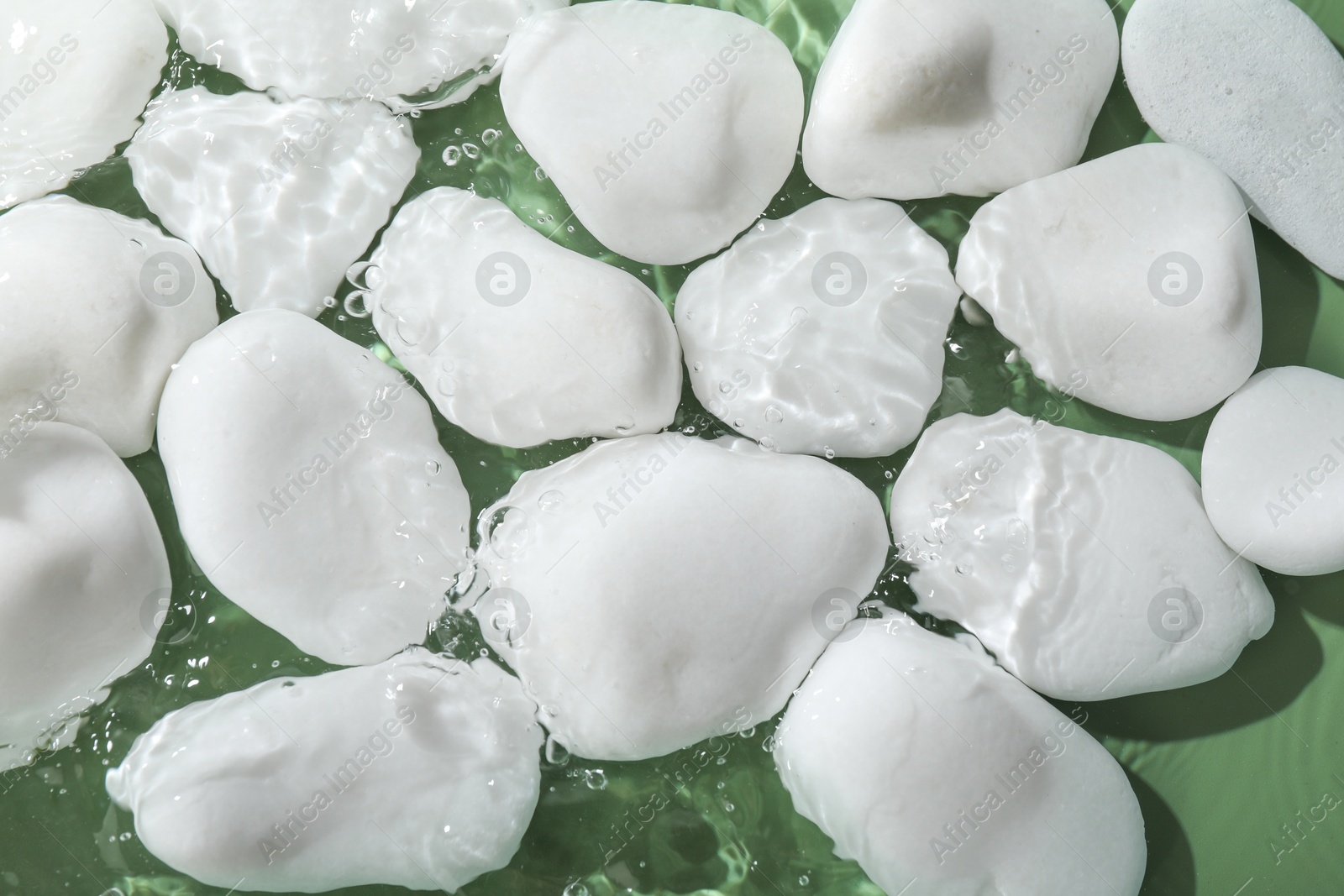 Photo of Spa stones in water on light green background, flat lay