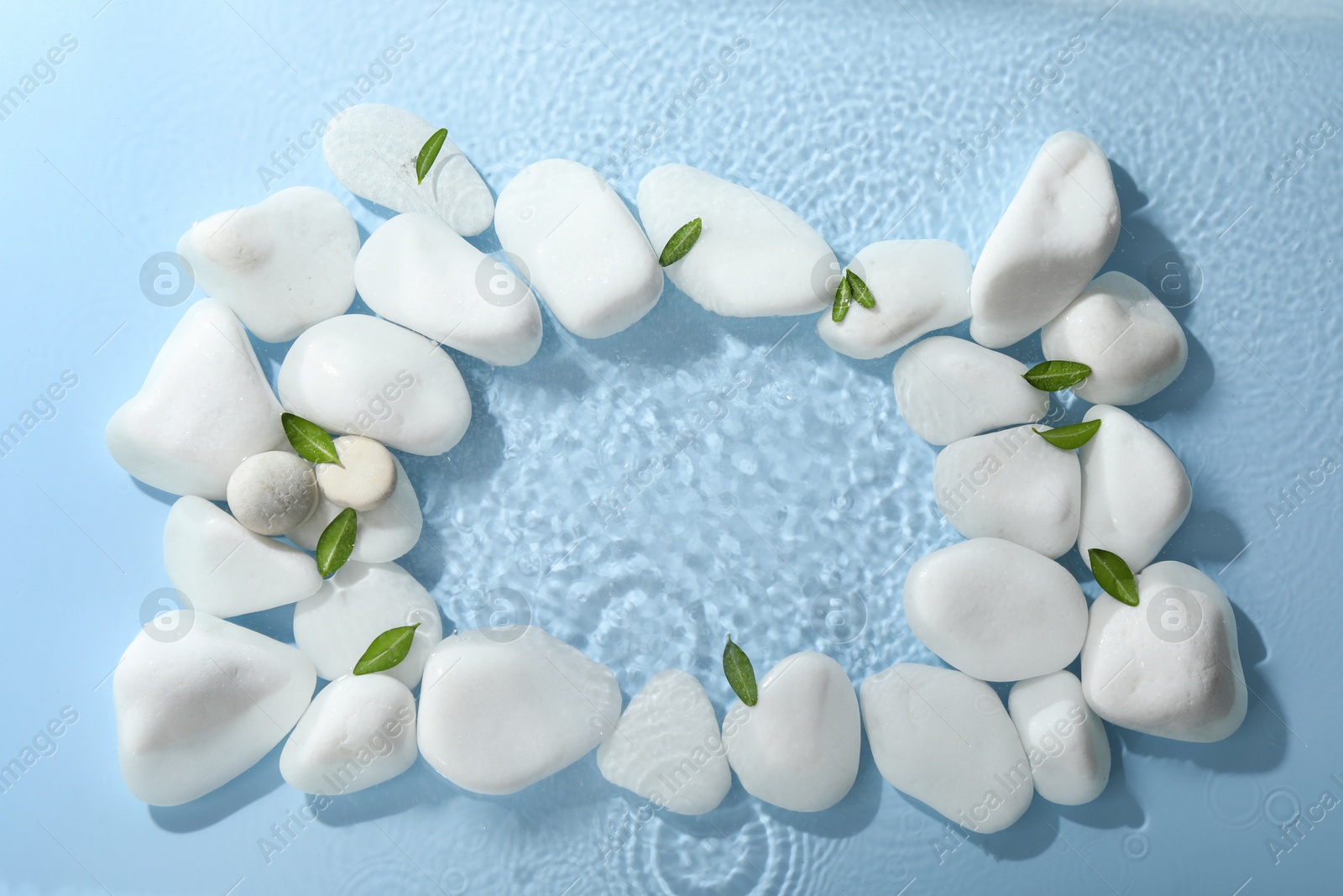 Photo of Frame made of spa stones and green leaves in water on light blue background, flat lay. Space for text