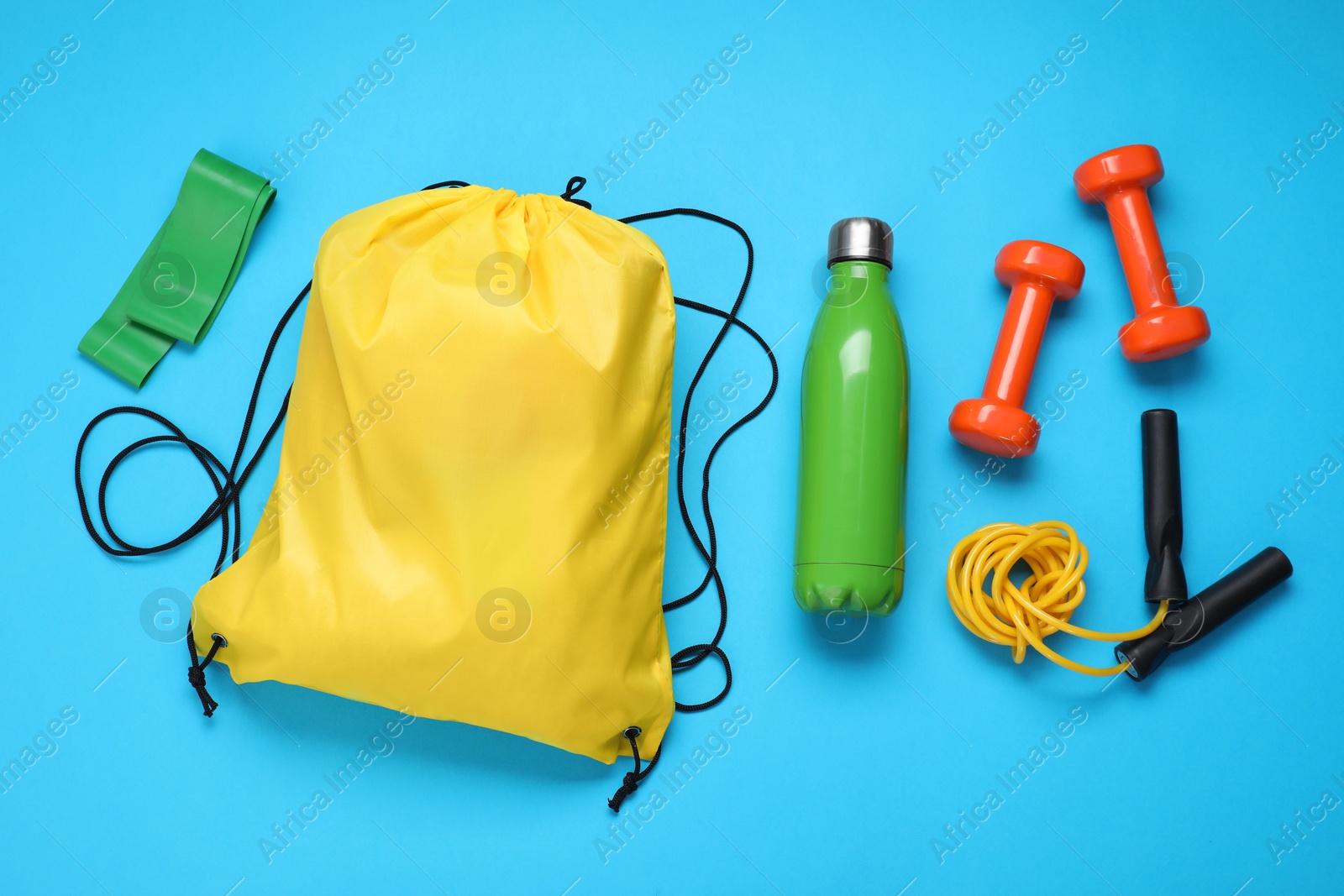 Photo of Yellow drawstring bag and sports equipment on light blue background, flat lay