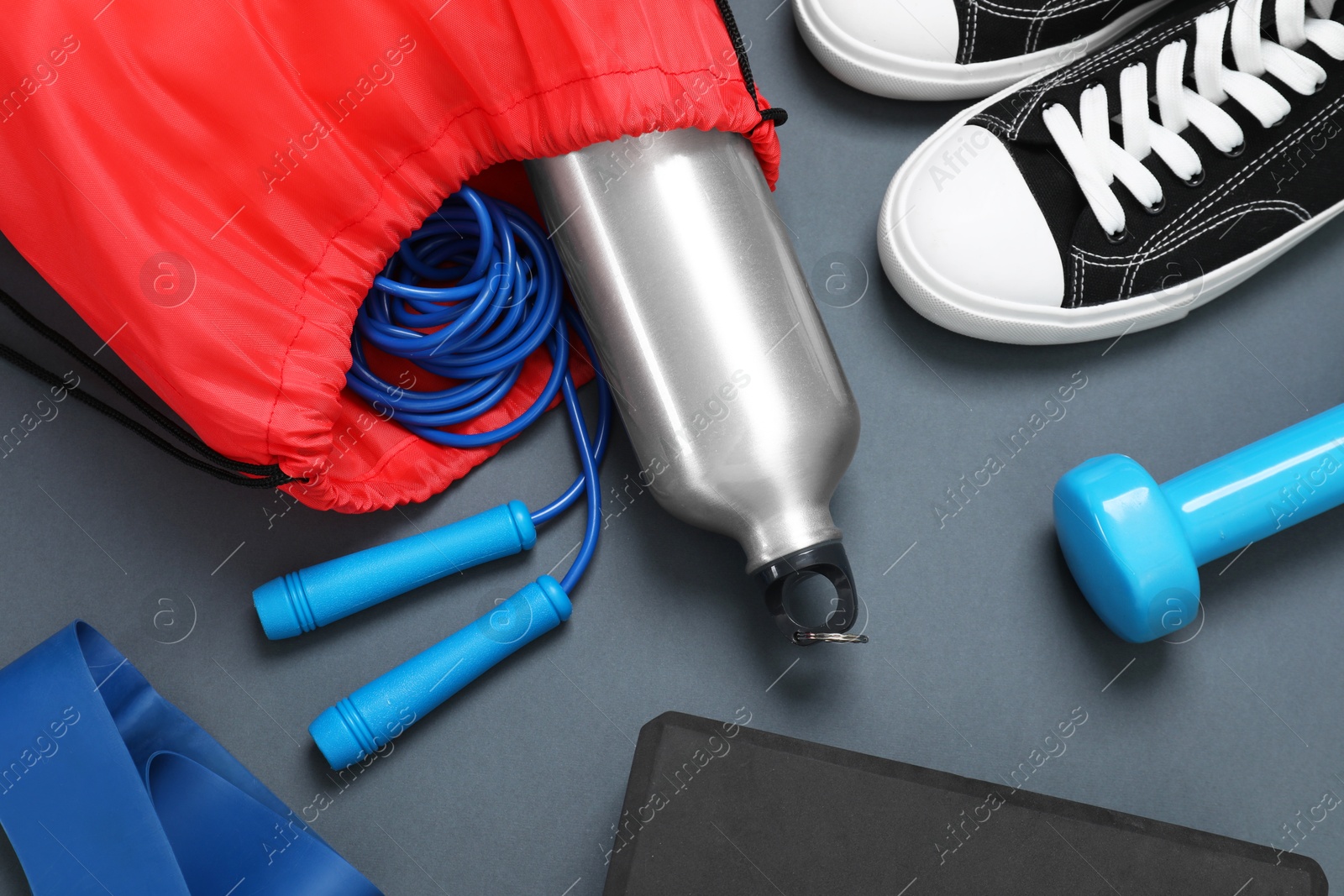Photo of Red drawstring bag, sneakers and sports equipment on grey background, flat lay