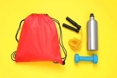 Red drawstring bag and sports equipment on yellow background, flat lay