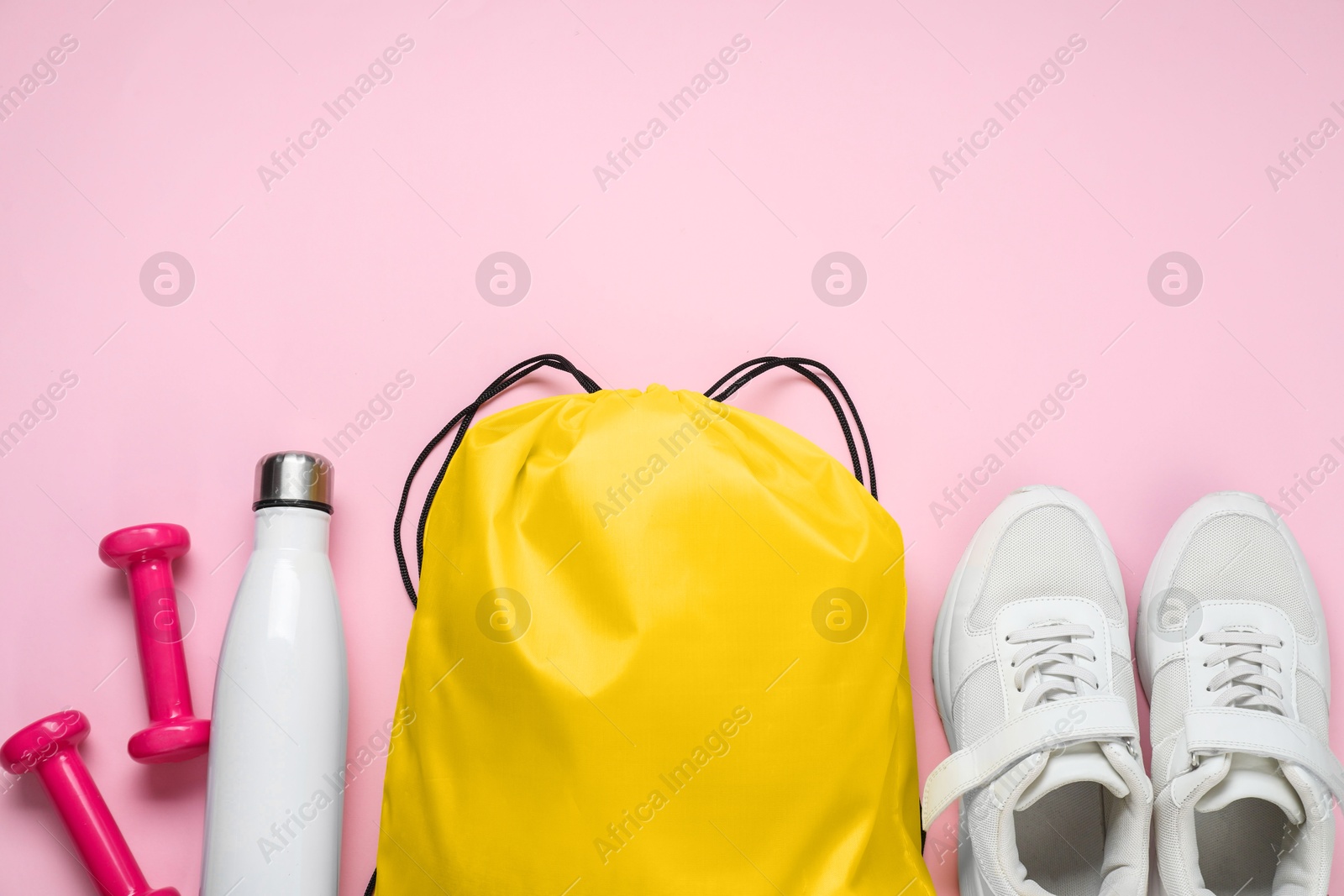 Photo of Yellow drawstring bag, sneakers, thermo bottle and dumbbells on pink background, flat lay. Space for text