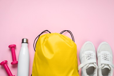 Yellow drawstring bag, sneakers, thermo bottle and dumbbells on pink background, flat lay. Space for text