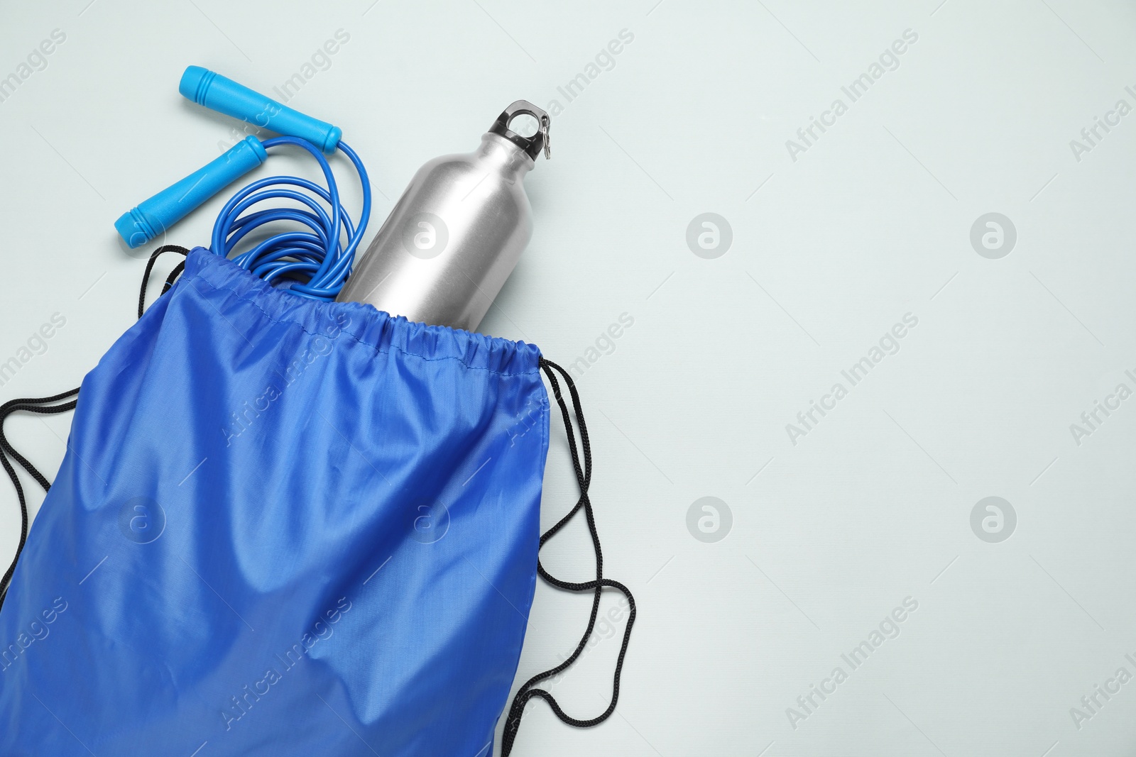 Photo of Blue drawstring bag, thermo bottle and skipping rope on grey background, top view. Space for text
