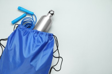 Blue drawstring bag, thermo bottle and skipping rope on grey background, top view. Space for text