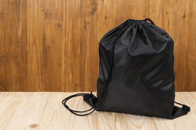 Photo of Black drawstring bag on light wooden table. Space for text