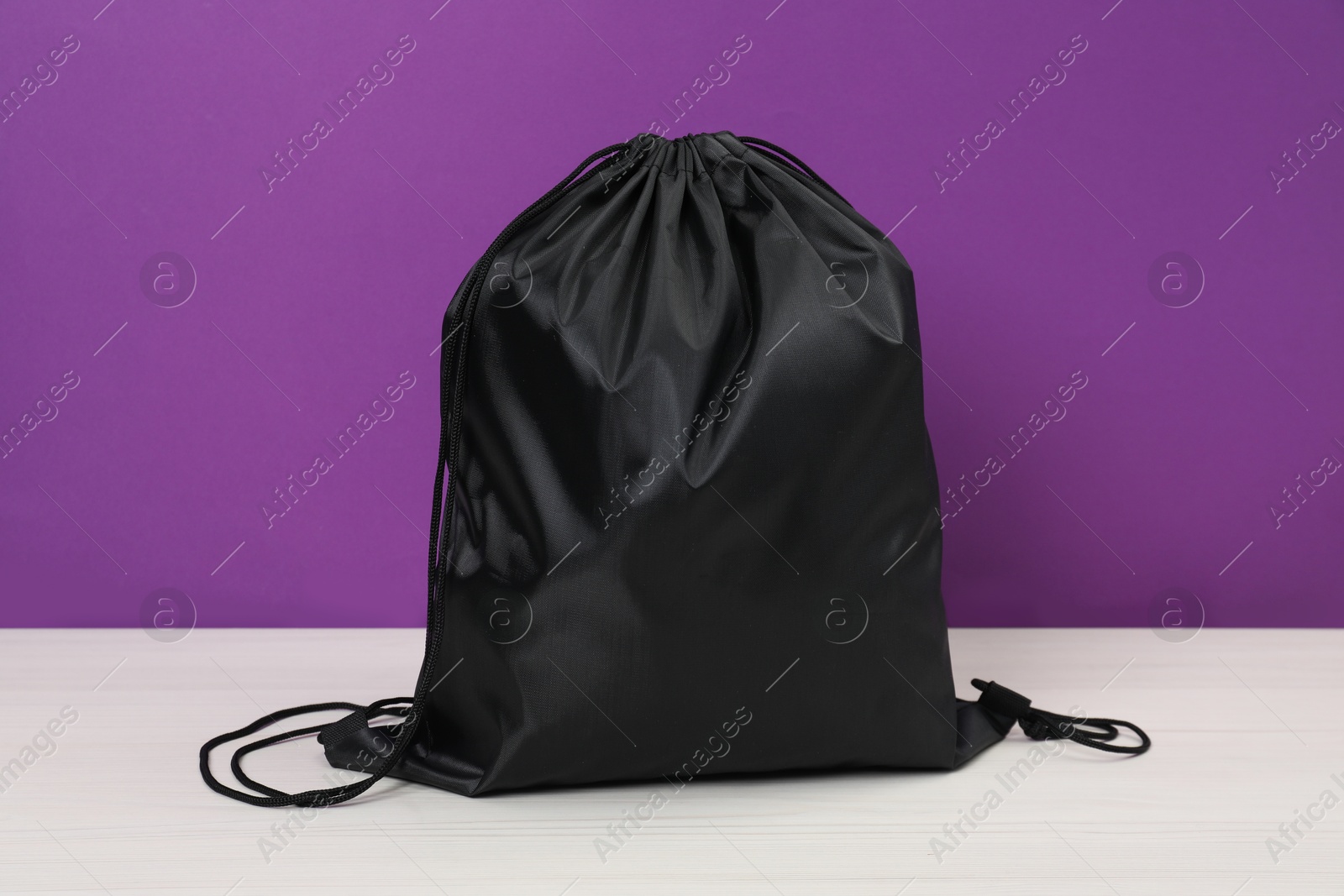 Photo of Black drawstring bag on white wooden table against purple background