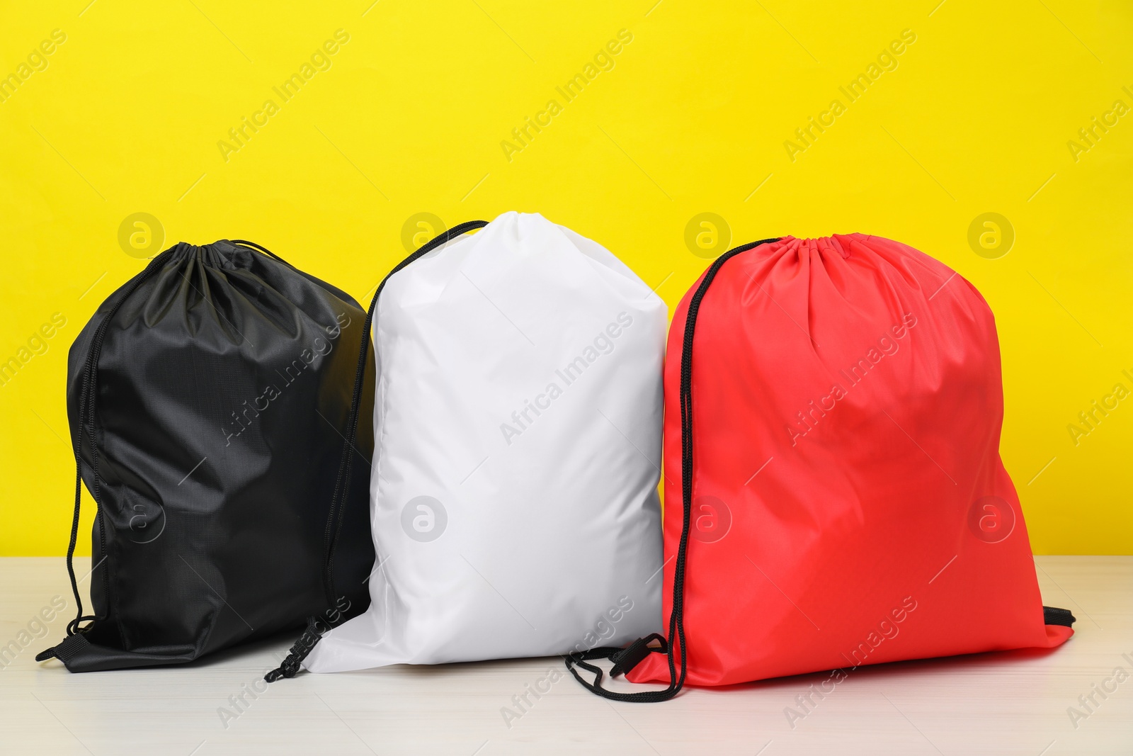 Photo of Three drawstring bags on white wooden table against yellow background