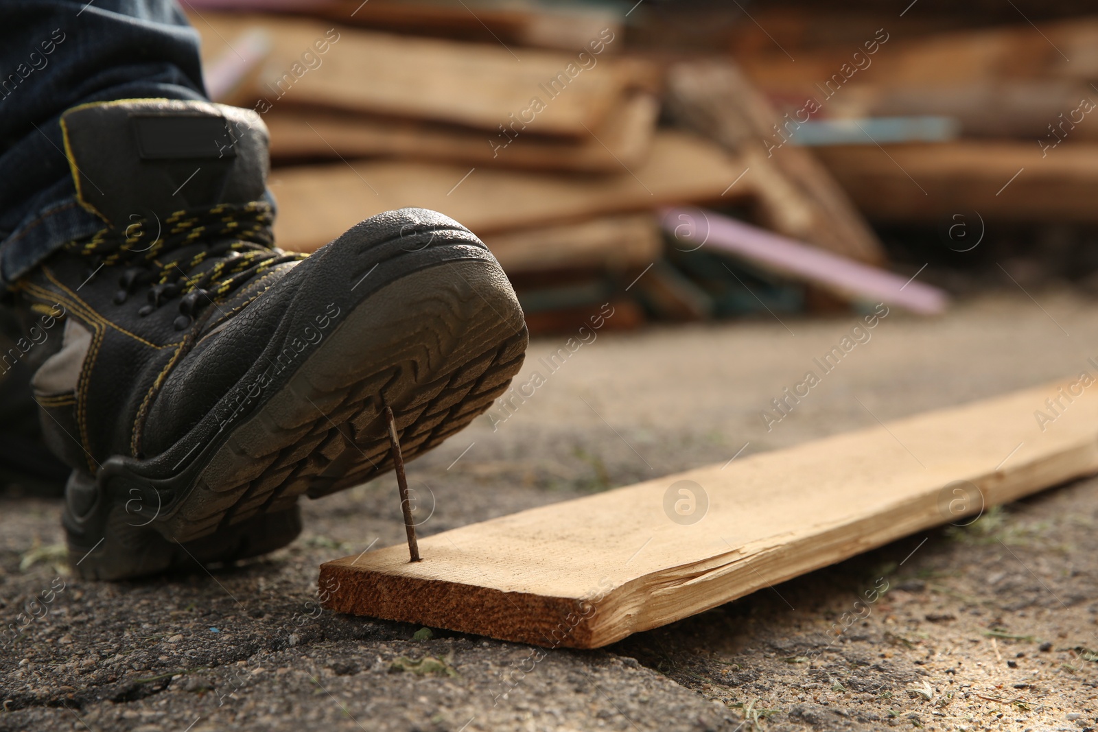 Photo of Careless worker stepping on nail in wooden plank outdoors, closeup