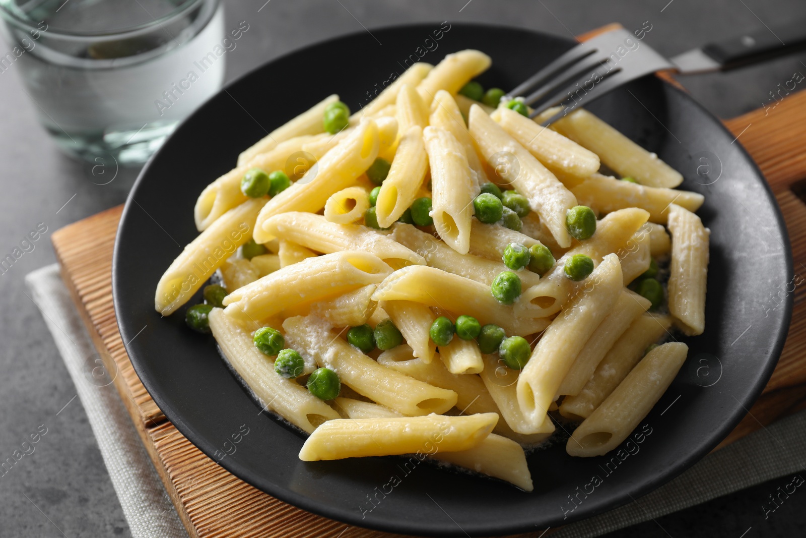 Photo of Delicious pasta with green peas, cheese, fork and water on grey table, closeup