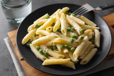 Photo of Delicious pasta with green peas, cheese, fork and water on grey table, closeup