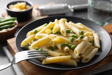 Delicious pasta with green peas, cheese and fork on table, closeup