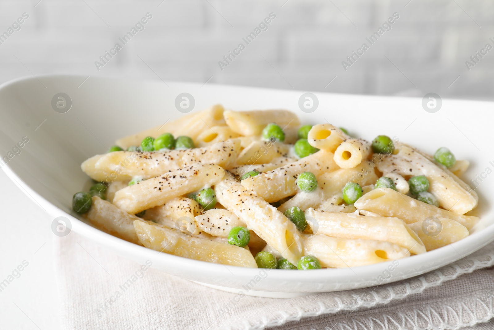 Photo of Delicious pasta with green peas and creamy sauce in bowl on table, closeup