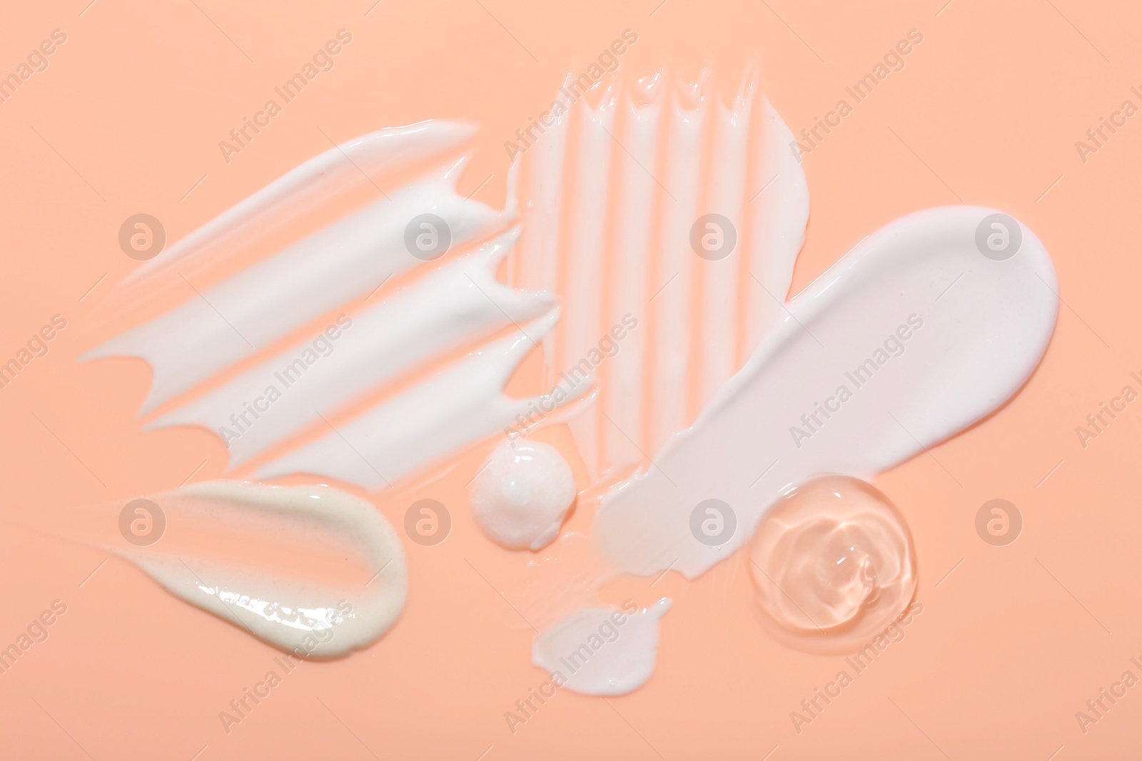 Photo of Samples of face cream on coral background, top view