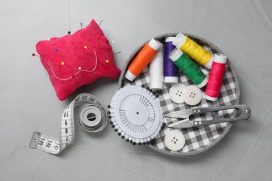 Photo of Red pincushion with pins and other sewing tools on grey table, flat lay