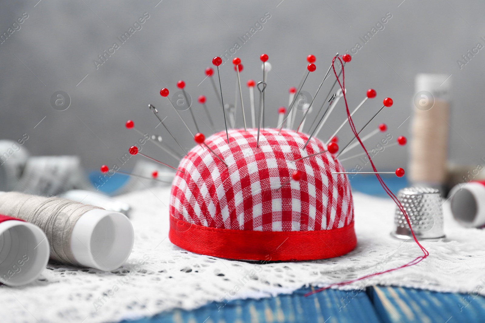 Photo of Checkered pincushion with pins and other sewing tools on blue wooden table, closeup