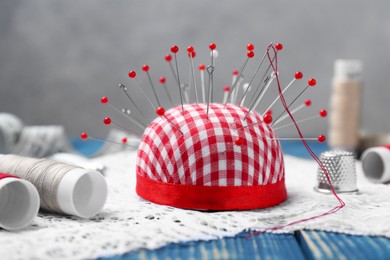 Photo of Checkered pincushion with pins and other sewing tools on blue wooden table, closeup