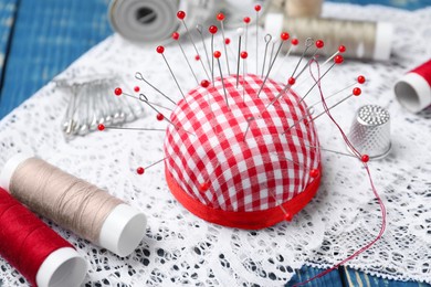 Photo of Checkered pincushion with pins and other sewing tools on blue wooden table, closeup