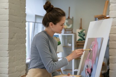 Woman drawing beautiful flamingo with brush in studio
