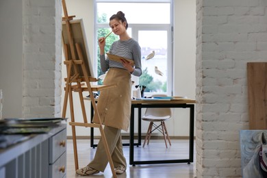 Photo of Woman drawing on easel with canvas in studio