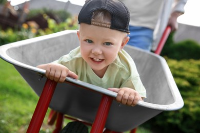 Photo of Father pushing wheelbarrow with his son outdoors, closeup